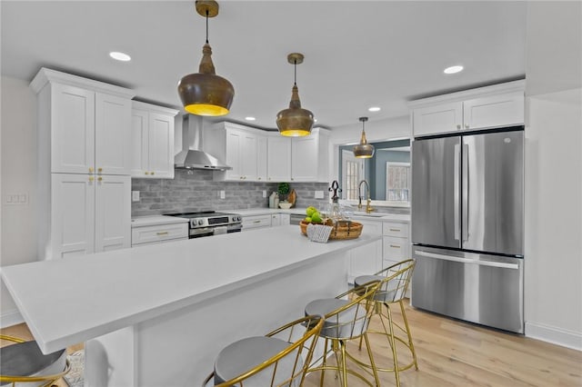 kitchen with light countertops, wall chimney exhaust hood, appliances with stainless steel finishes, and a sink