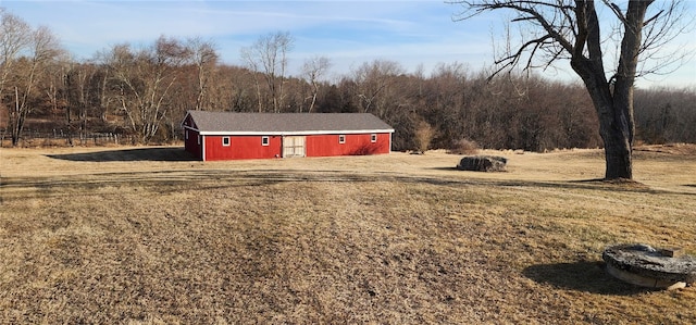 exterior space featuring a detached garage, an outbuilding, a view of trees, and dirt driveway