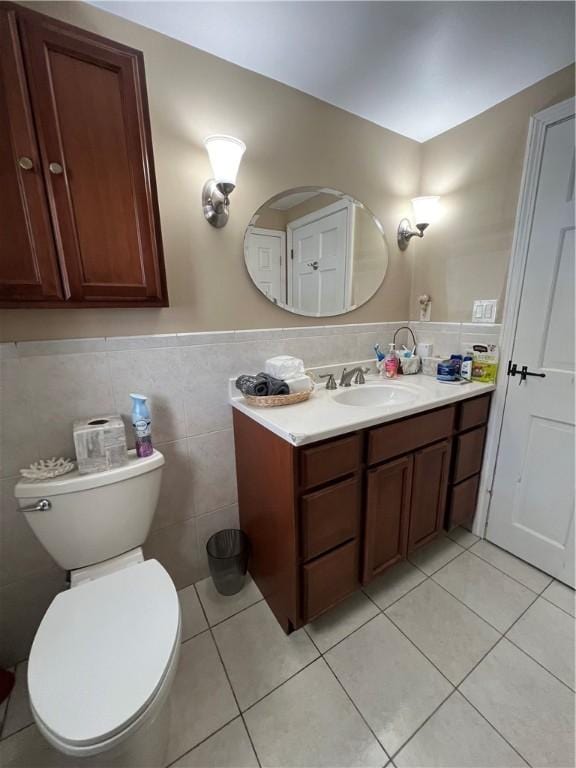 half bathroom featuring a wainscoted wall, toilet, tile walls, tile patterned flooring, and vanity