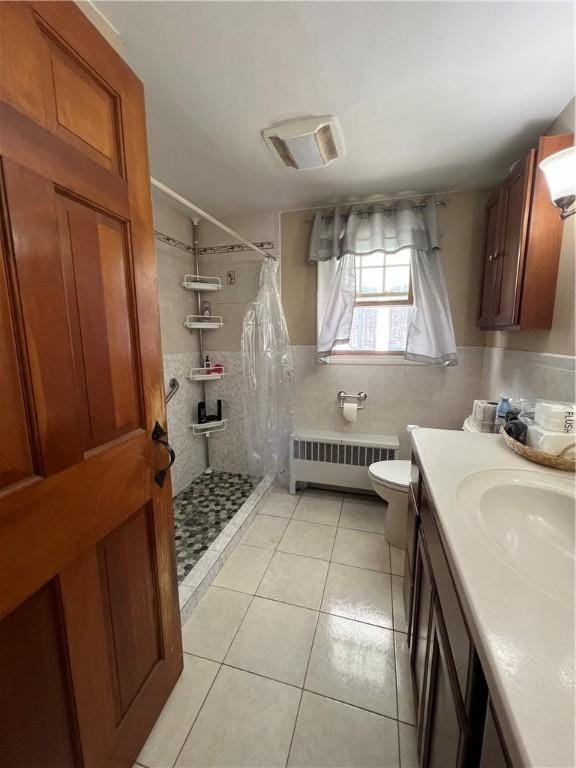 full bath with tile patterned floors, toilet, a tile shower, radiator, and tile walls