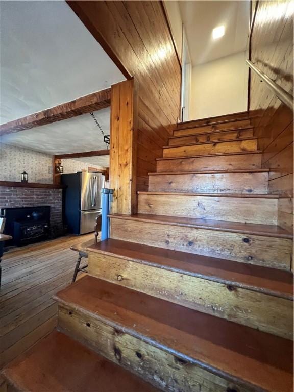 staircase with wooden walls, a brick fireplace, and hardwood / wood-style flooring