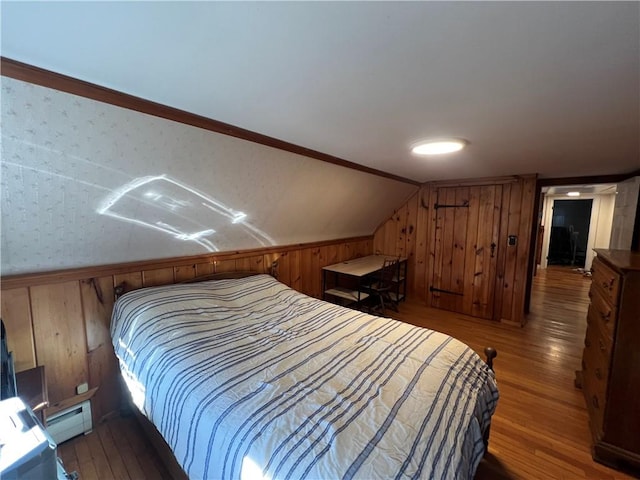 bedroom featuring vaulted ceiling, a baseboard heating unit, wooden walls, and wood finished floors