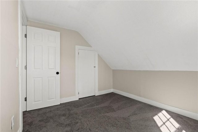 additional living space featuring baseboards, lofted ceiling, and dark colored carpet