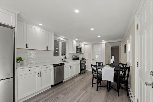 kitchen with a baseboard radiator, light countertops, light wood-style floors, stainless steel appliances, and a sink