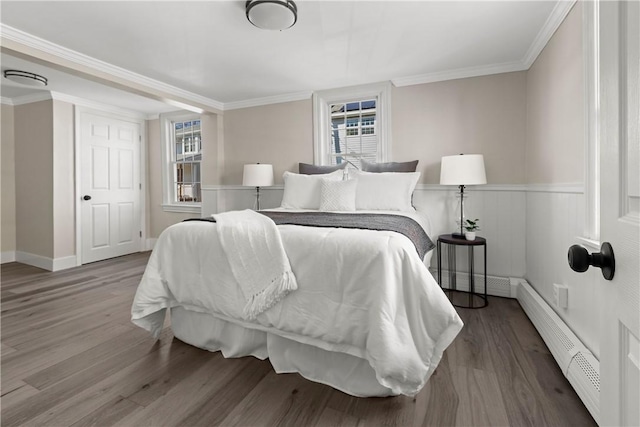 bedroom with ornamental molding, wood finished floors, wainscoting, and a baseboard radiator