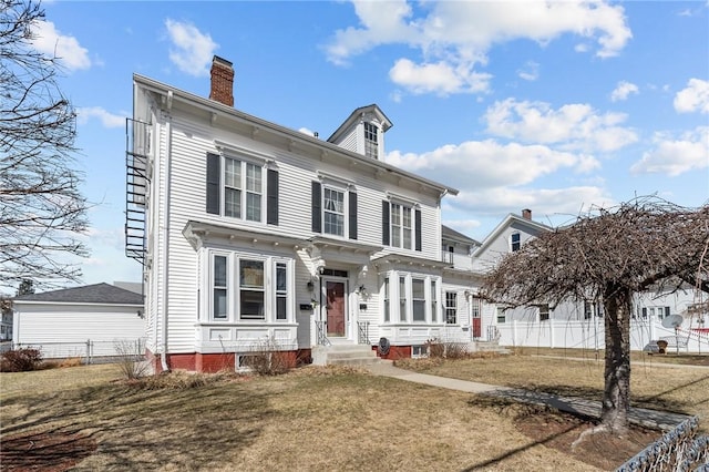 italianate-style house featuring a front lawn, a chimney, and fence