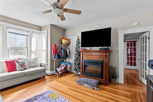 living area featuring a glass covered fireplace, wood finished floors, and ceiling fan