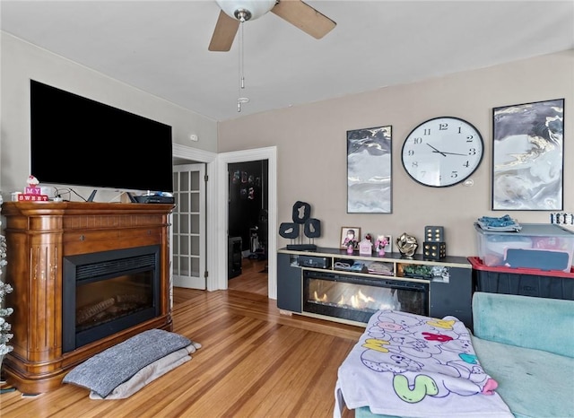 living area featuring a glass covered fireplace, a ceiling fan, and wood finished floors