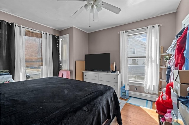 bedroom with ceiling fan, baseboard heating, wood finished floors, and crown molding