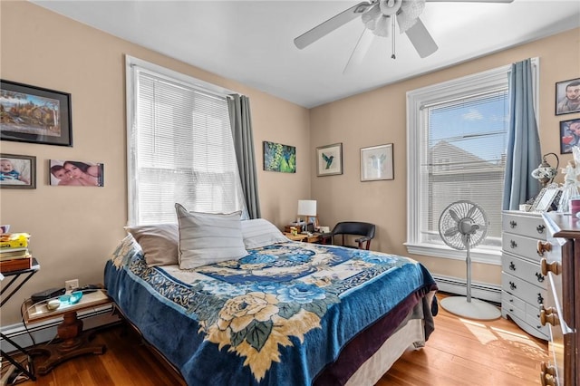 bedroom with multiple windows, wood finished floors, baseboard heating, and ceiling fan