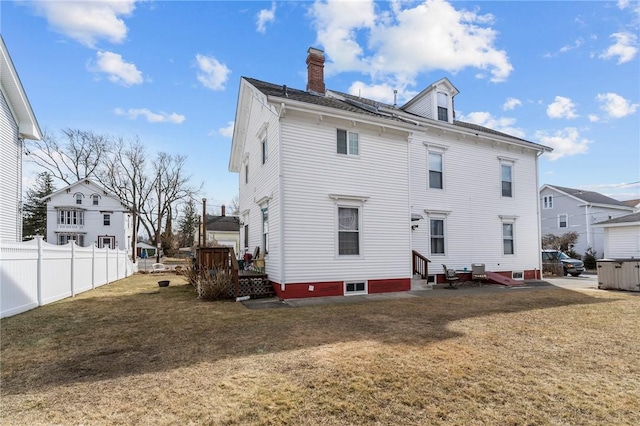 rear view of house with a lawn, entry steps, a chimney, and fence