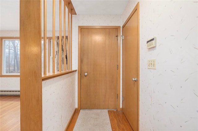 doorway to outside featuring a baseboard radiator, baseboards, wood finished floors, and wallpapered walls