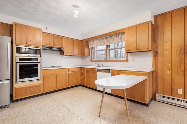 kitchen with under cabinet range hood, appliances with stainless steel finishes, brown cabinetry, light countertops, and baseboard heating