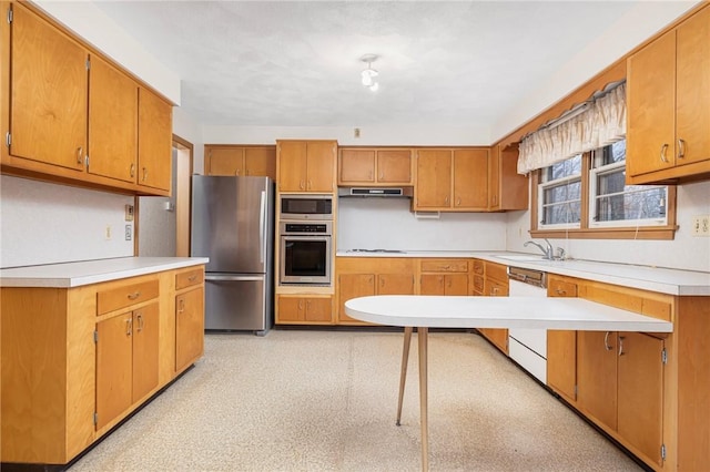 kitchen featuring under cabinet range hood, light floors, light countertops, appliances with stainless steel finishes, and brown cabinetry