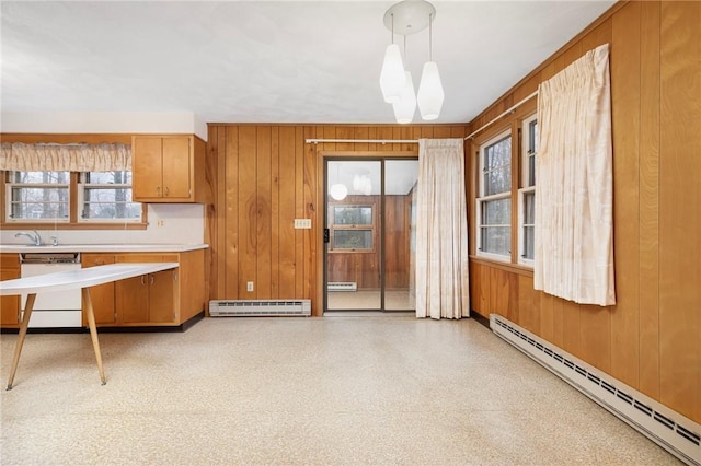 kitchen featuring wooden walls, brown cabinetry, light countertops, baseboard heating, and dishwasher