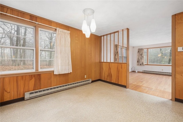 unfurnished room featuring a baseboard heating unit, baseboard heating, a healthy amount of sunlight, and wood walls