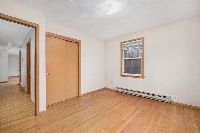 spare room featuring a baseboard heating unit, baseboards, and light wood-type flooring