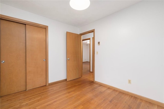 unfurnished bedroom featuring a closet, baseboards, and light wood finished floors