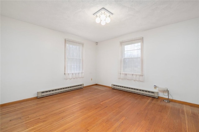 spare room featuring a baseboard heating unit, light wood-style floors, baseboards, and a baseboard radiator