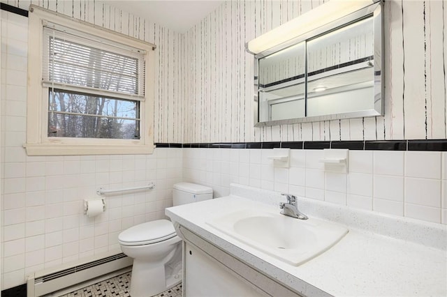 bathroom featuring wallpapered walls, wainscoting, a baseboard heating unit, tile walls, and toilet