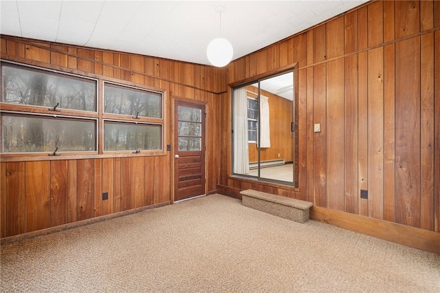 carpeted spare room featuring wooden walls and baseboard heating