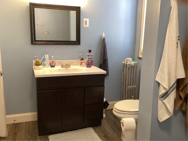 half bathroom featuring radiator, vanity, baseboards, and wood finished floors