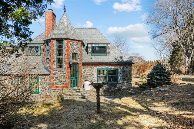 view of front of home with entry steps, stone siding, a patio, roof with shingles, and a chimney