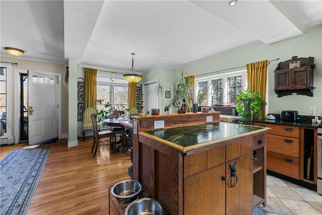 kitchen with baseboards, light wood-style floors, dark countertops, brown cabinets, and a center island