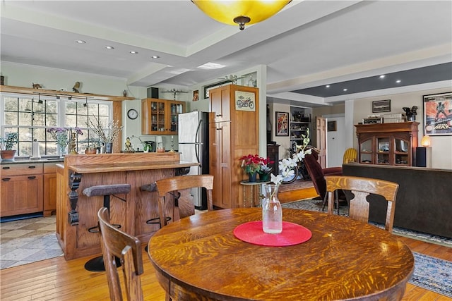 dining area with recessed lighting, light wood-style floors, crown molding, indoor wet bar, and a raised ceiling