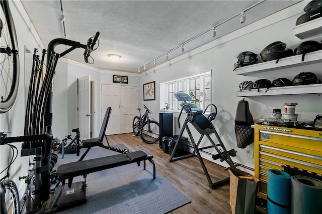 exercise room with track lighting, ornamental molding, a textured ceiling, and wood finished floors