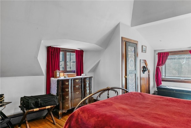 bedroom with a baseboard radiator, lofted ceiling, and wood finished floors