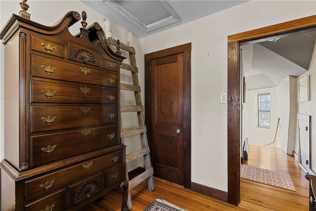 hall with baseboards, light wood-style floors, and attic access