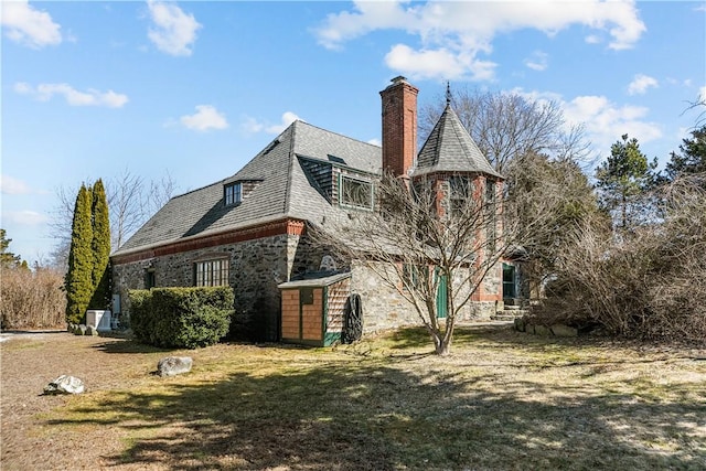 view of side of home with a yard, stone siding, and a chimney