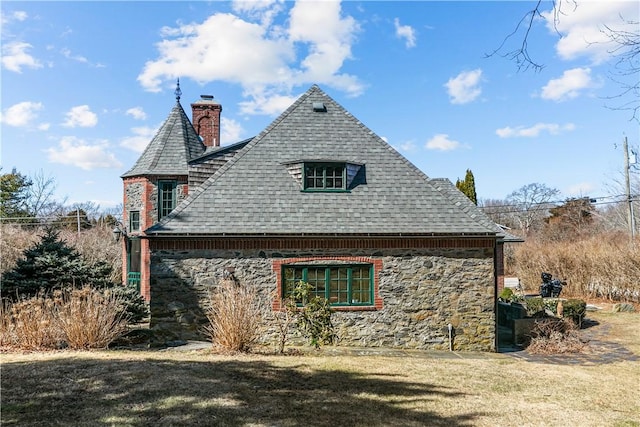 view of side of home with a yard, stone siding, a chimney, and a shingled roof