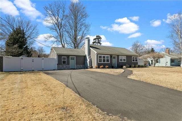 ranch-style home with a gate, aphalt driveway, stone siding, fence, and a chimney