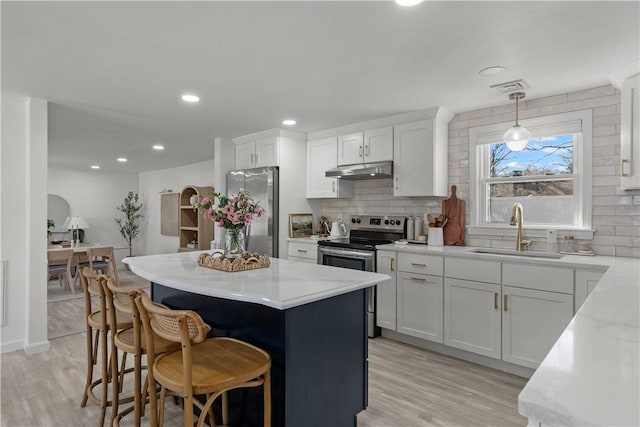 kitchen featuring visible vents, a sink, under cabinet range hood, tasteful backsplash, and appliances with stainless steel finishes