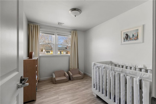 bedroom with visible vents, baseboards, a nursery area, and wood finished floors