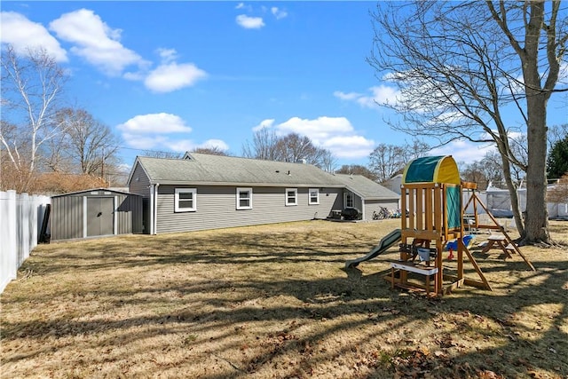 back of house with an outbuilding, fence, a playground, a yard, and a storage shed