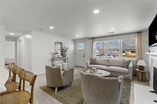 living room featuring light wood finished floors, a fireplace with flush hearth, recessed lighting, and baseboards