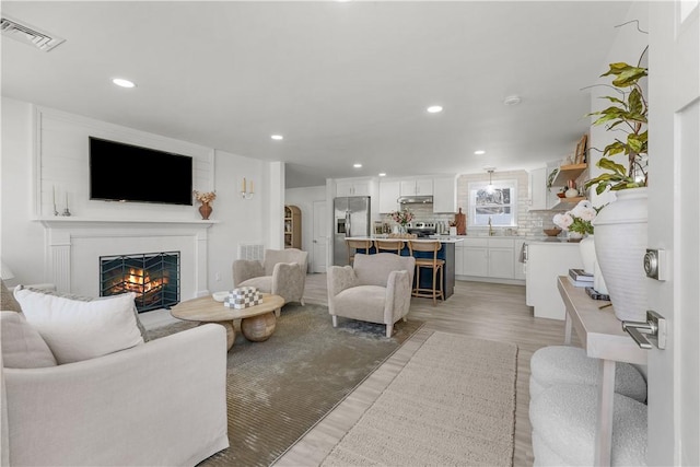 living room with visible vents, recessed lighting, light wood-style floors, and a lit fireplace