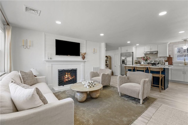 living area with light wood-style flooring, recessed lighting, visible vents, and a warm lit fireplace