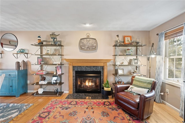 living area featuring a fireplace with flush hearth, light wood-type flooring, and baseboards