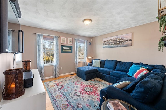 living area featuring light wood-type flooring, baseboards, a textured ceiling, and visible vents