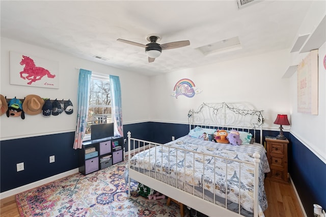 bedroom featuring visible vents, ceiling fan, attic access, wainscoting, and wood finished floors