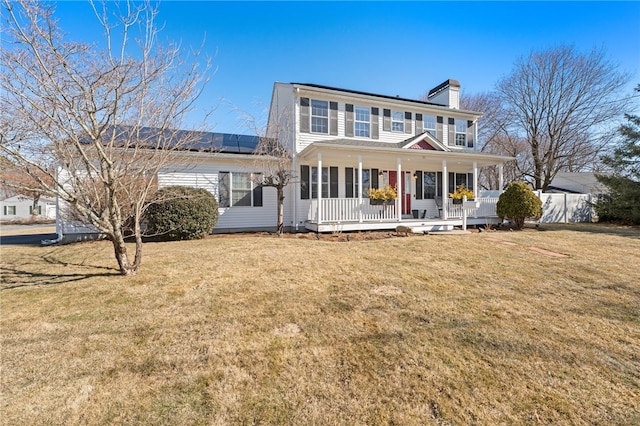 view of front of house featuring a front yard, covered porch, roof mounted solar panels, and a chimney