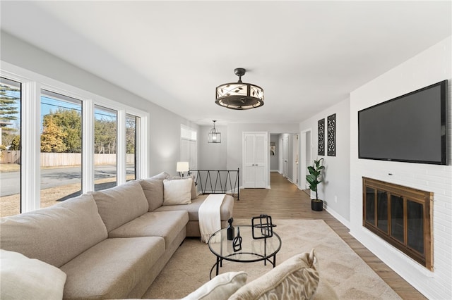 living room featuring a brick fireplace, baseboards, and wood finished floors