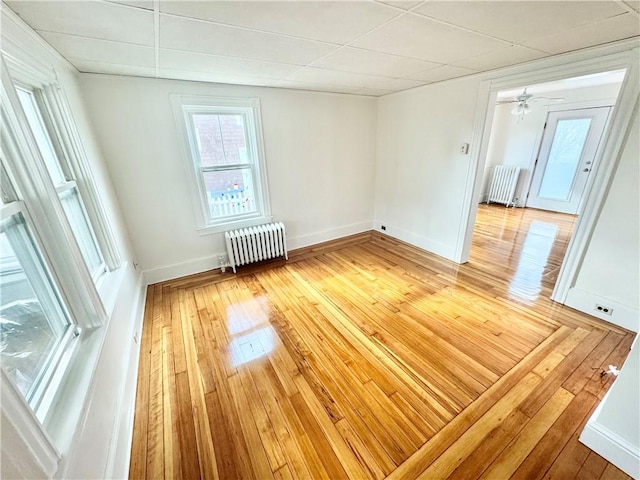 spare room with radiator, a drop ceiling, light wood finished floors, and baseboards