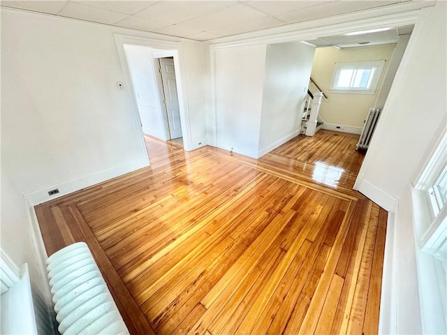 empty room featuring baseboards, stairs, radiator heating unit, and light wood-type flooring