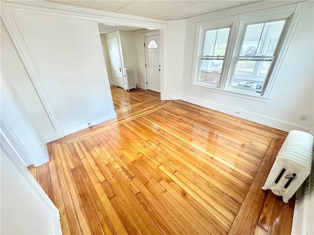 unfurnished room with light wood finished floors, baseboards, and radiator heating unit