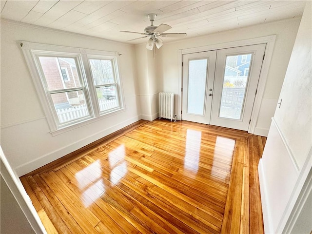 unfurnished room featuring french doors, light wood-style flooring, baseboards, radiator heating unit, and ceiling fan